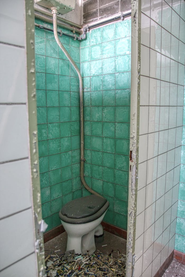 Home An abandoned restroom with green tiles and broken fixtures, revealing signs of decay.